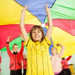 Smiling boys and girls playing parachute game